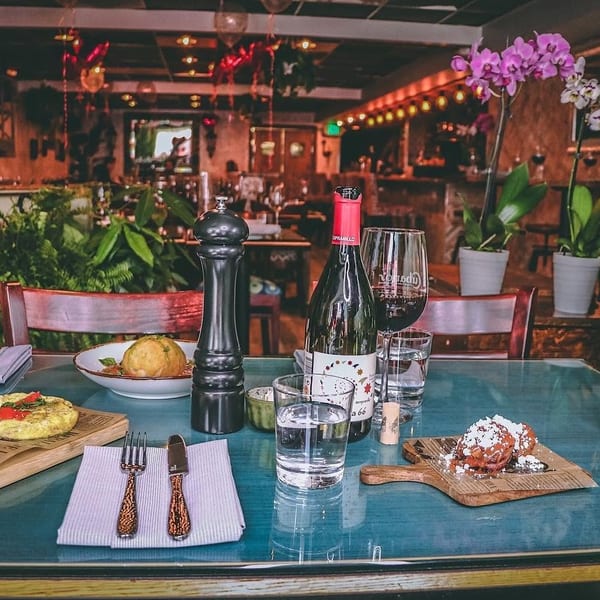 Table set with Cuban food, wine, and water glasses in a restaurant with lush greenery.
