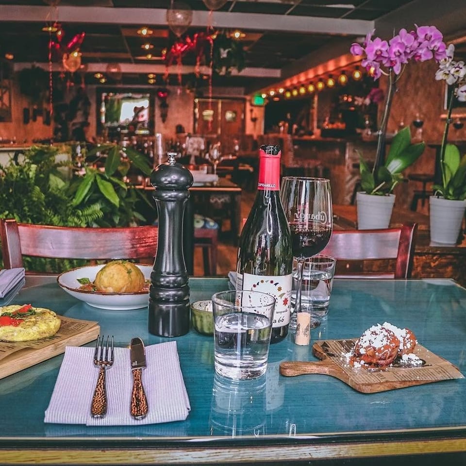 Table set with Cuban food, wine, and water glasses in a restaurant with lush greenery.