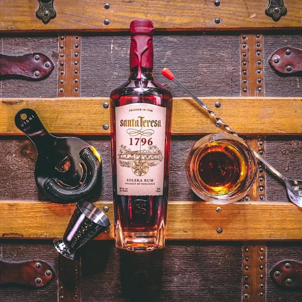 Santa Teresa 1796 Solera Rum bottle, glass, jigger, and bar tools on a vintage wooden trunk.