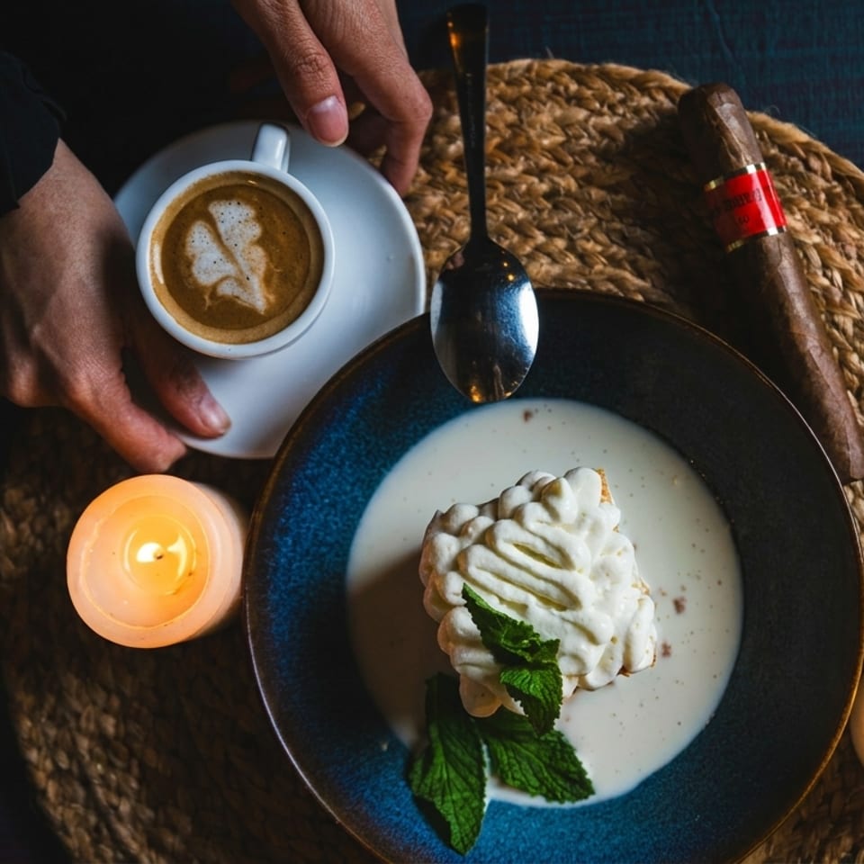 Overhead view of dessert, coffee, lit candles, and a cigar on a textured placemat.